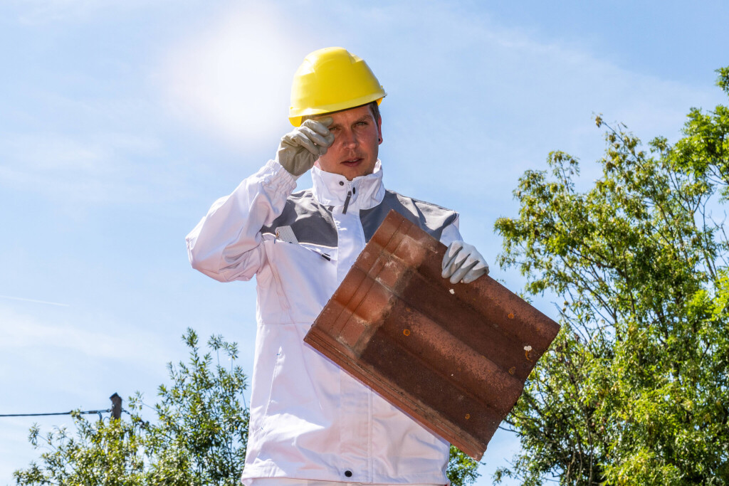 Ein Bauarbeiter auf dem Dach steht in der prallen Sonne während einer Hitzewelle. Das Bild verdeutlicht die körperliche Belastung, Risiken und Herausforderungen von Arbeiten im Sommer auf dem Bau.